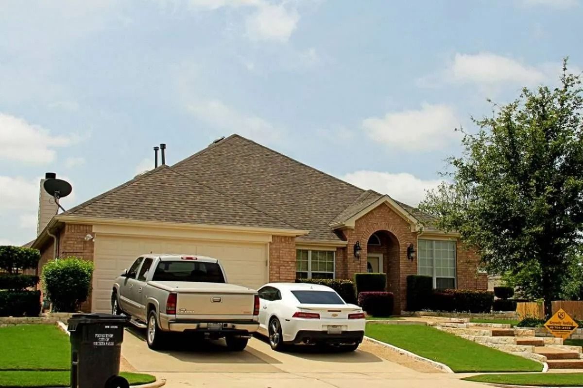 Suburban brick house with two parked vehicles and a trash bin in the driveway