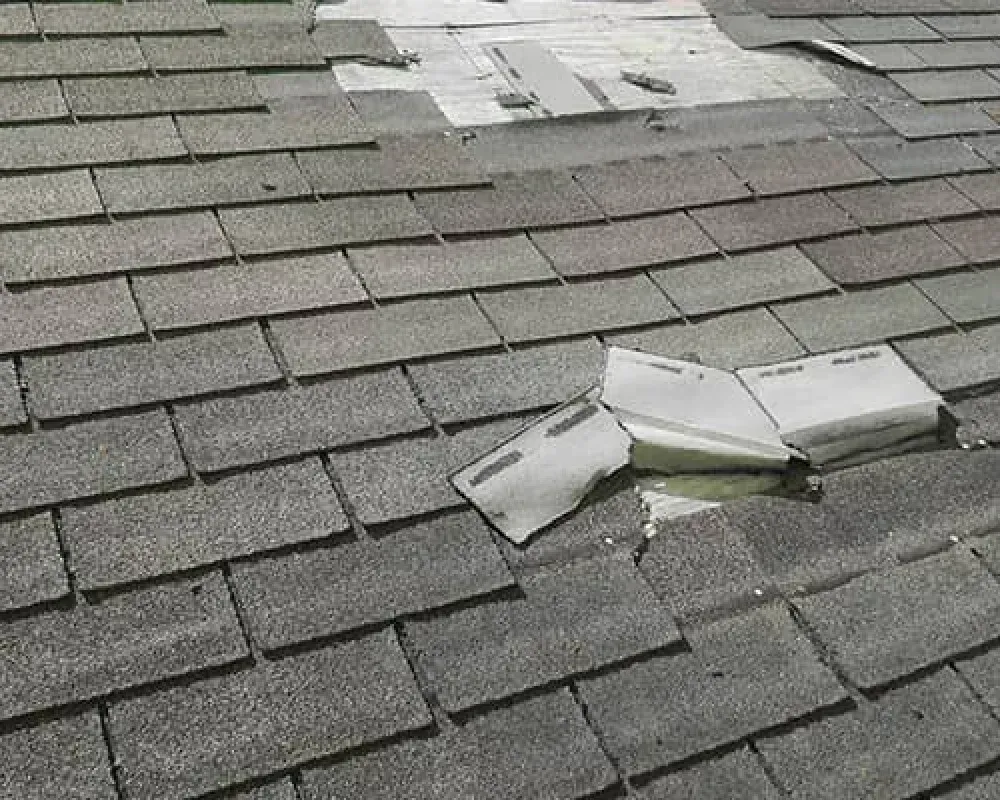 Damaged shingle roof with scattered broken pieces and a hole near the ridge