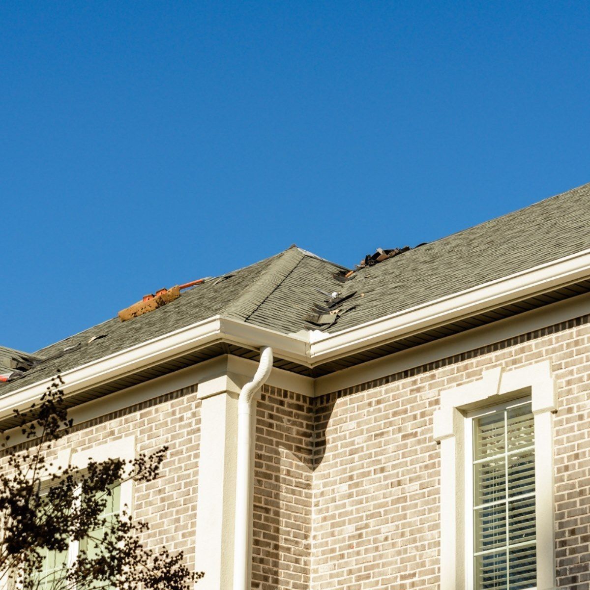 Damaged house roof with missing shingles under a clear blue sky
