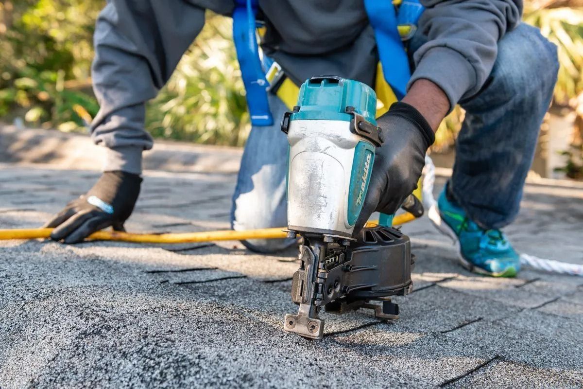 Worker using a nail gun to fasten roofing shingles on a roof