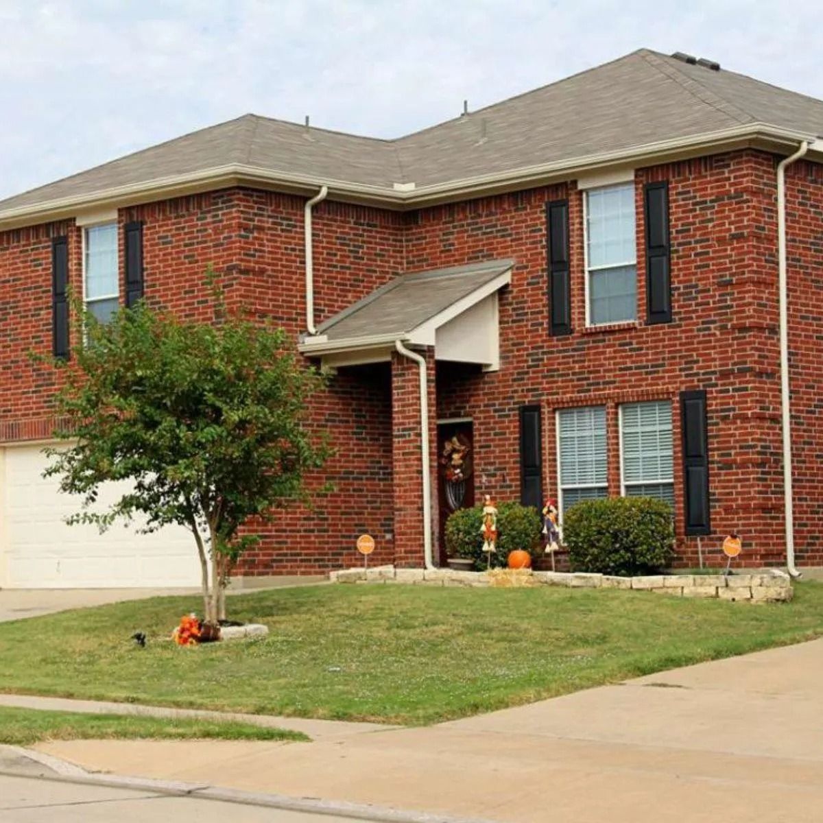 Two-story brick suburban house with a front lawn, tree, and driveway