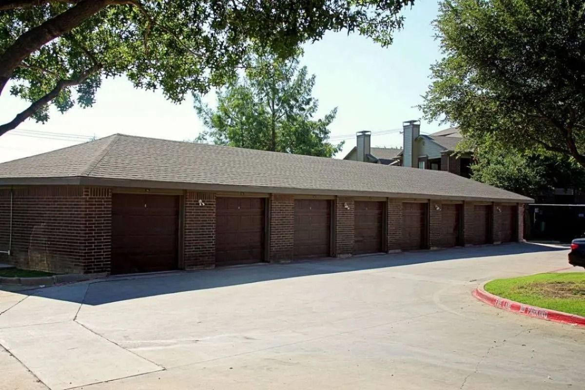 Low brick building with a row of garage doors beside a paved driveway and trees