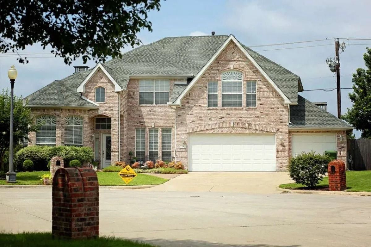 Large brick suburban house with a two-car garage and manicured lawn on a sunny day