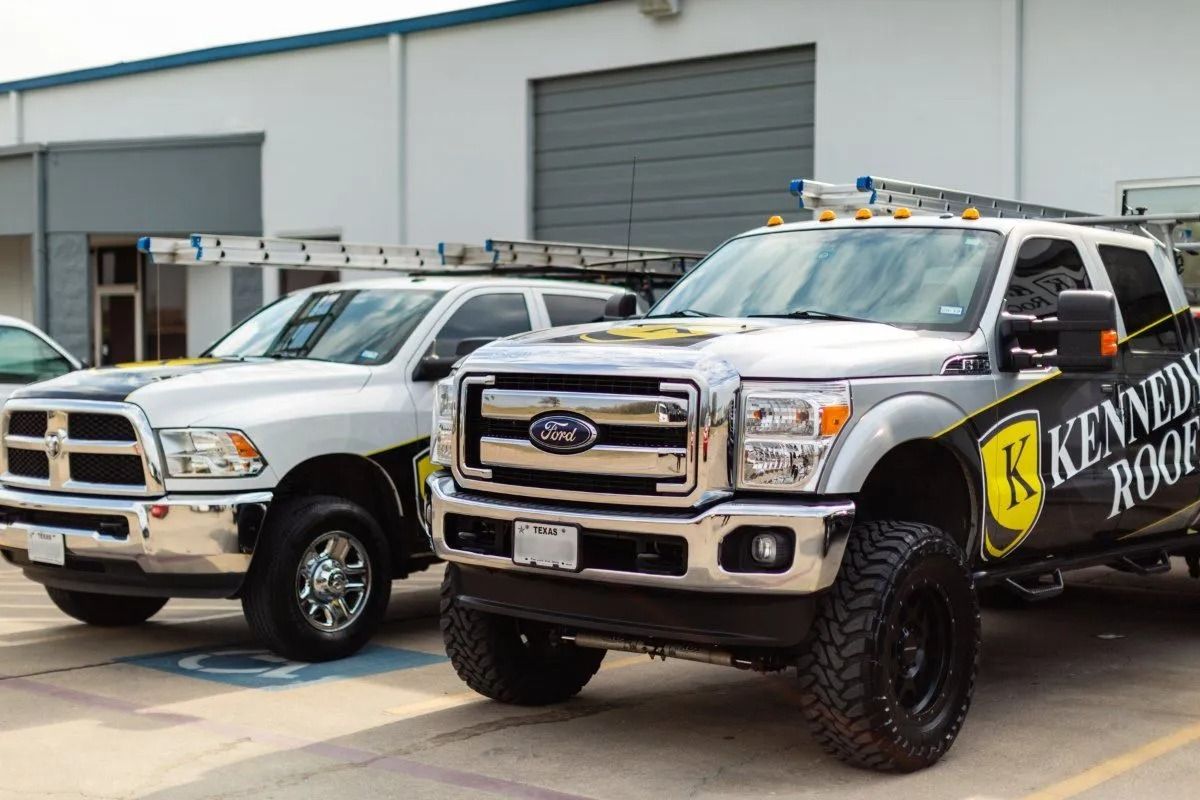 Two tow trucks parked outside a garage, one white and one black with a yellow logo.