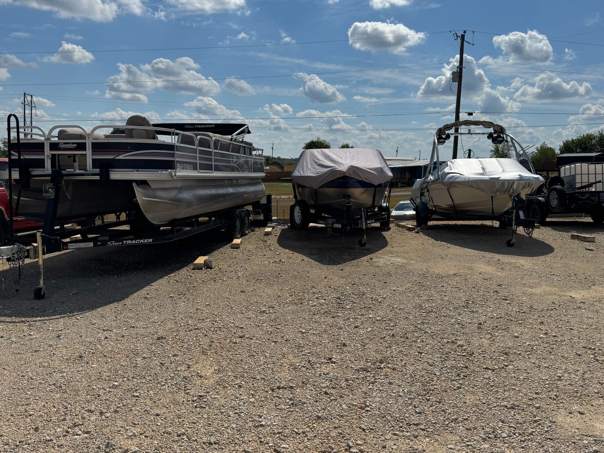 Boats on trailers in a gravel lot under a cloudy blue sky.