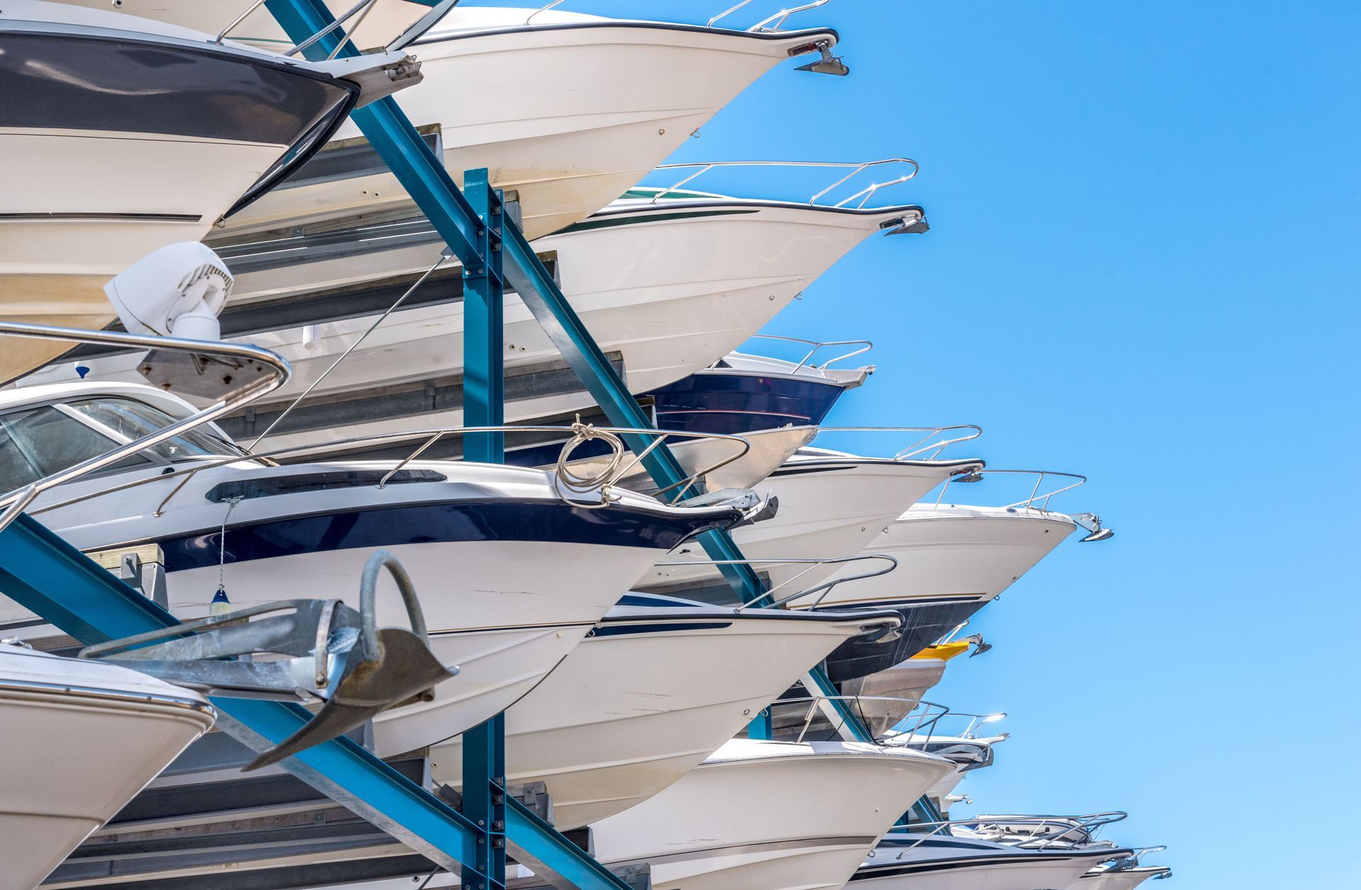 Boats stacked on a rack, against a bright blue sky.