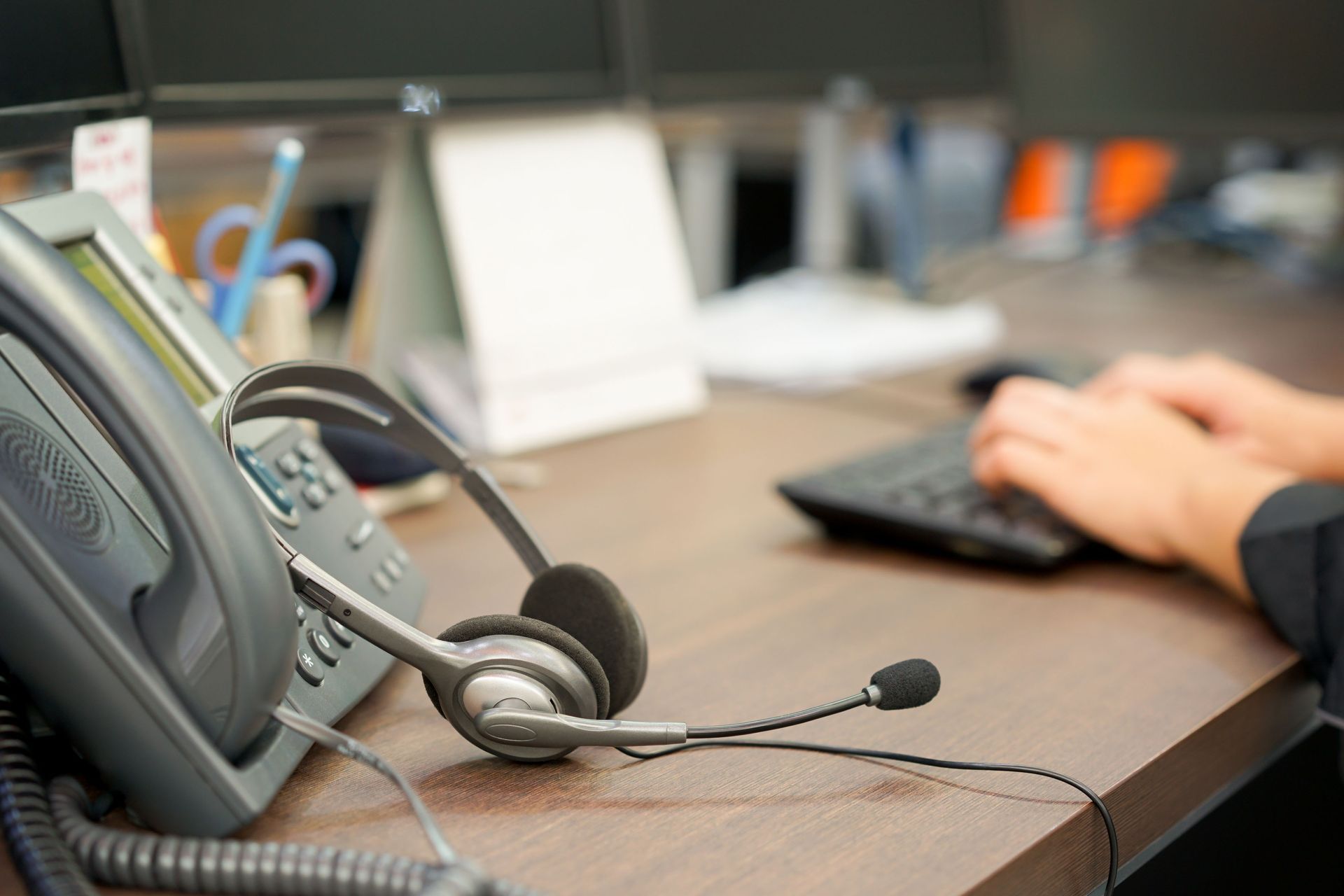 Headset on desk next to phone, keyboard and hands typing in office.