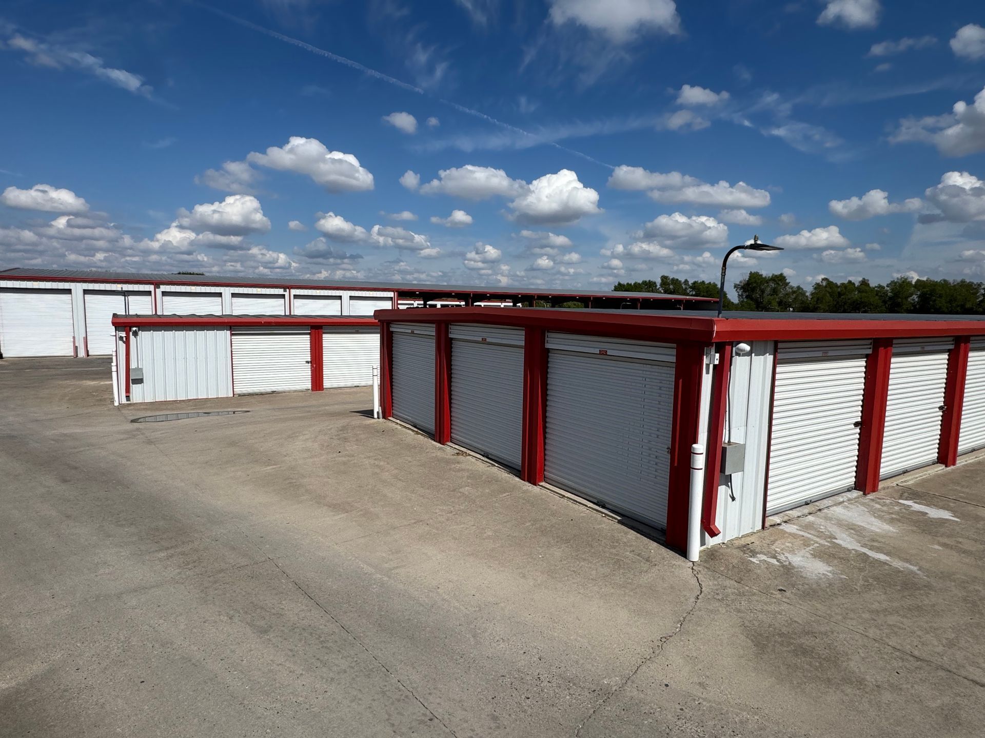 Storage units with white doors and red trim under a blue sky.