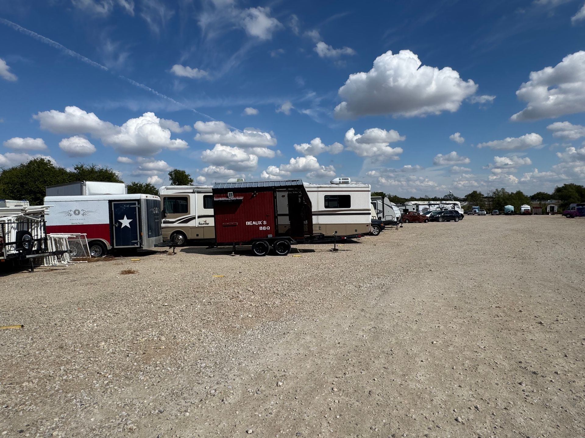 Campers parked on a gravel lot under a blue sky with scattered clouds.