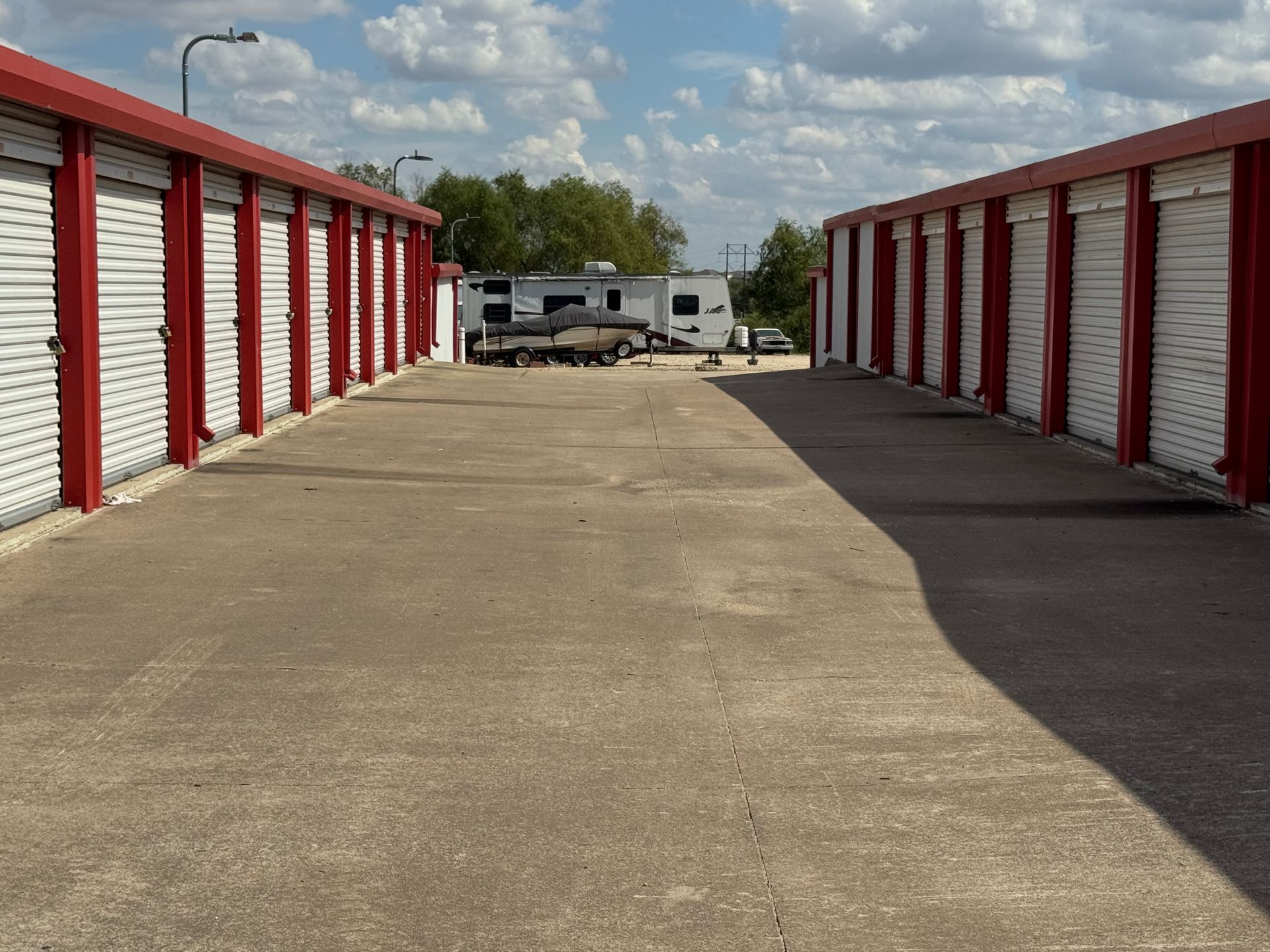 Rows of red and white storage units with a paved drive, vehicles in the distance.