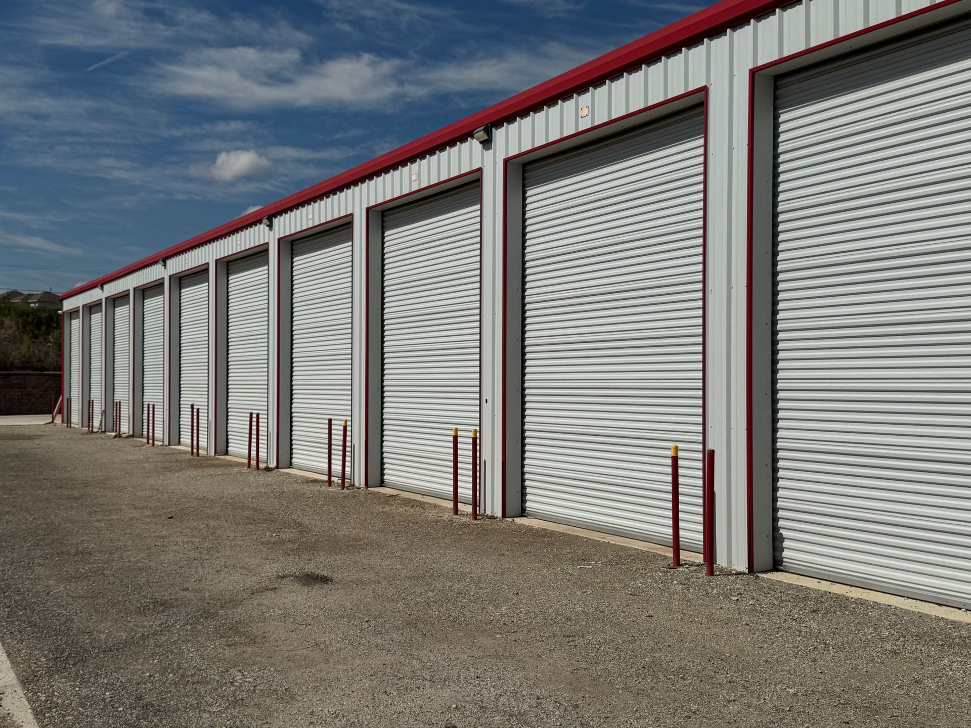 Row of white storage units with red trim, gravel ground, and blue sky.