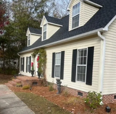 Beige house with black shutters, a dark roof, and brick steps.