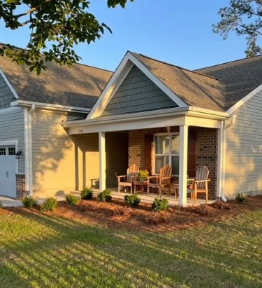 Exterior of a house with a covered porch, tan siding, and a green gable. Chairs are on the porch.
