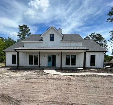 White farmhouse with black trim, a blue door, and porch under a blue sky.