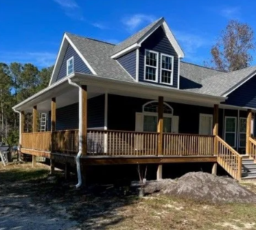 Blue house with a wraparound porch and wooden railings on a sunny day.