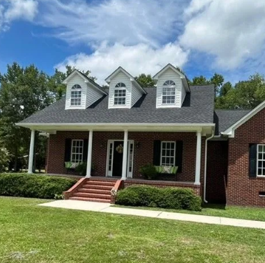 Brick house with a dark roof, white trim, and a porch under a blue sky.