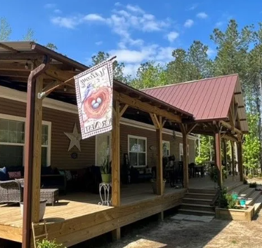 Brown house with porch, red metal roof, and bird nest flag under a blue sky.