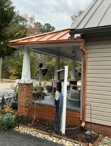 Copper-roofed porch with brick and white pillars, copper gutters, and a light tan building.