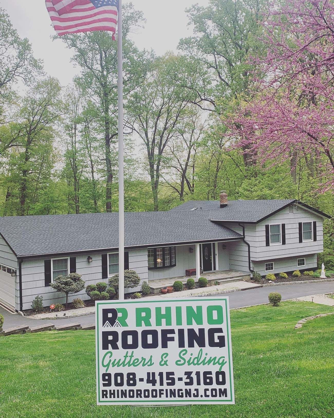 A house with a newly shingled roof, a Rhino Roofing sign, and a US flag.
