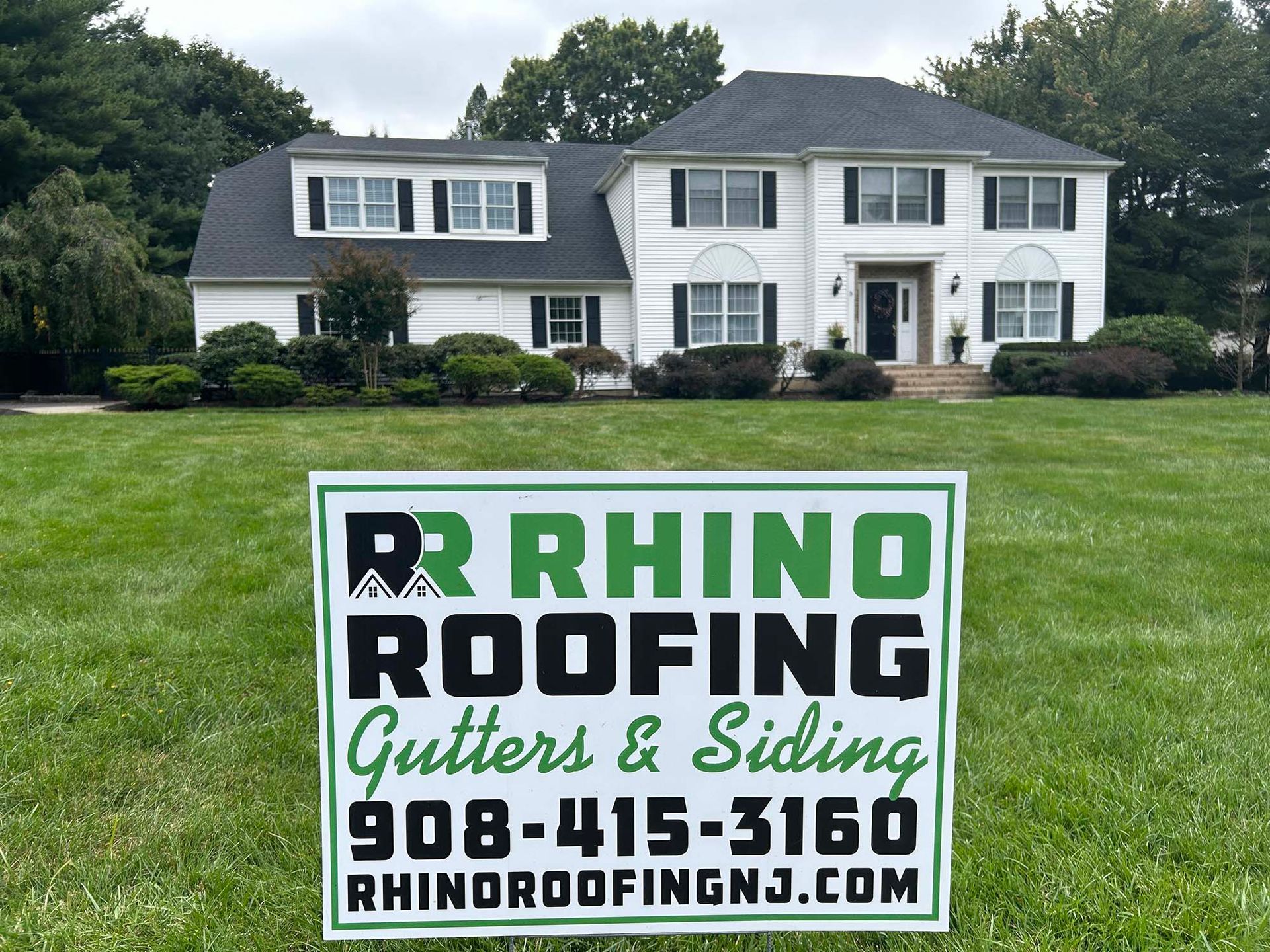 Sign in front of white house for Rhino Roofing, Gutters & Siding, with contact info.