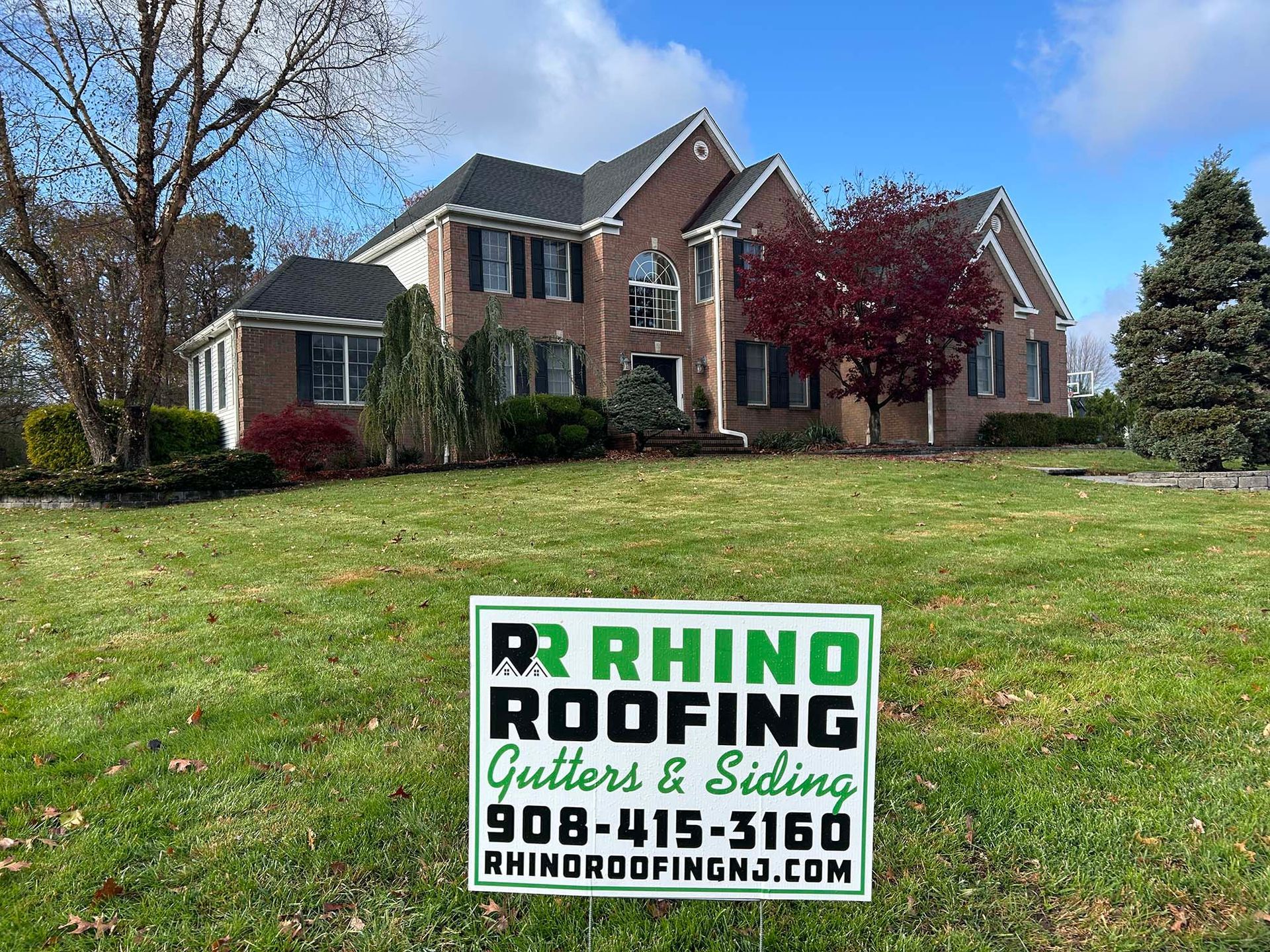 A two-story brick house with Rhino Roofing sign in front yard.