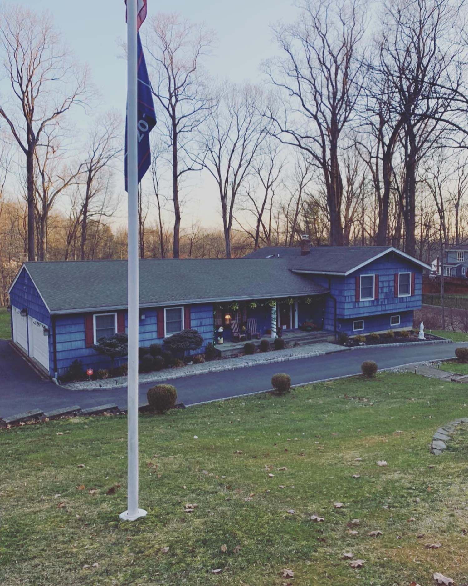 Blue house with a long driveway, flag pole, and bare trees in the background.