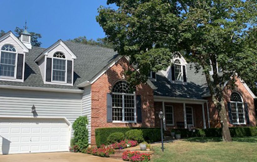 Two-story brick house with gray siding, black shutters, and arched windows, with a tree in front.