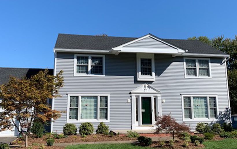 Two-story house with gray siding, white trim, and a dark green door under a blue sky.