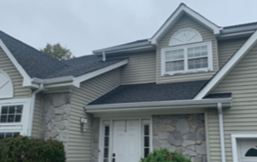 House exterior with dark roof, light siding, stone accents, white trim, and a cloudy sky.