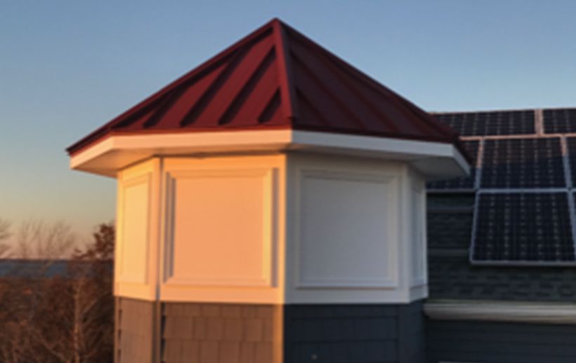 Red-roofed turret on a building with solar panels. The turret has white panels and a gray base.