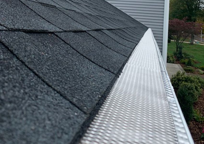 Close-up of a roof with black shingles and a silver gutter guard.