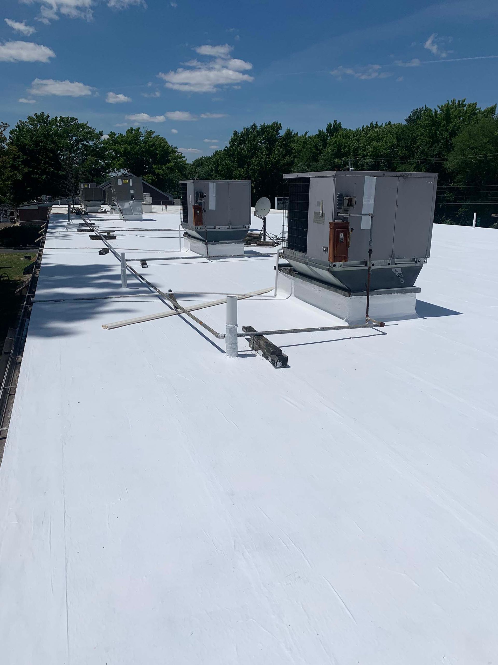 White commercial flat roof with HVAC units under a blue sky.