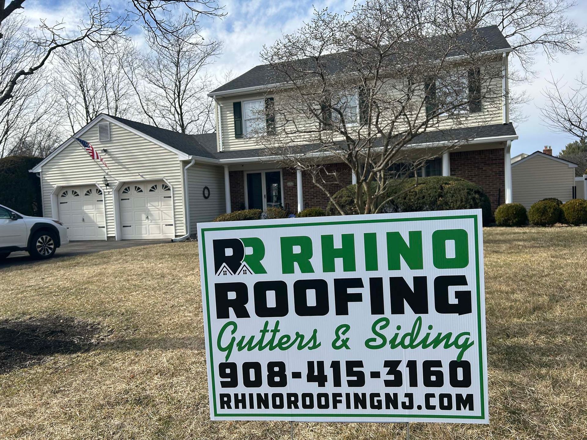 Rhino Roofing sign in front of a two-story house with a white garage.