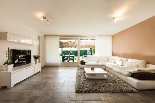 Modern living room with white sectional sofa, TV console, and sliding doors to a patio and garden.