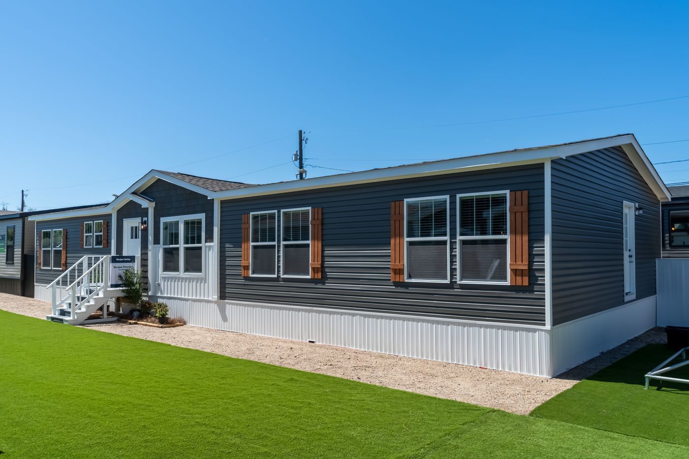 Exterior of a blue mobile home with white trim and a green lawn under a clear sky