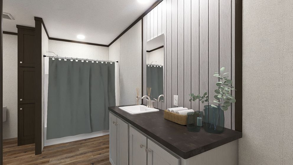 Modern bathroom with gray tiled walls, dark vanity, mirror, sink, and shower curtain over wood flooring.