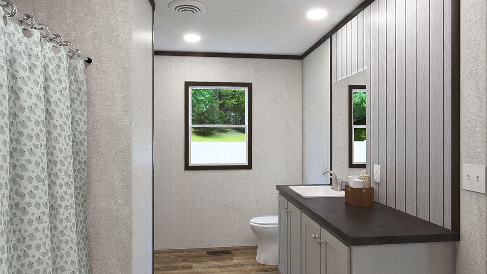 Bright bathroom with gray vanity, shower curtain, toilet, and window overlooking greenery
