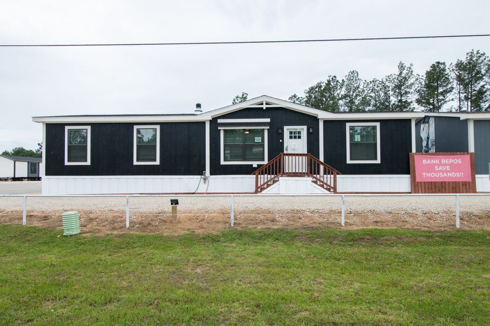 Small black-and-white modular building with a front porch and pink sign, set on a grassy lot.