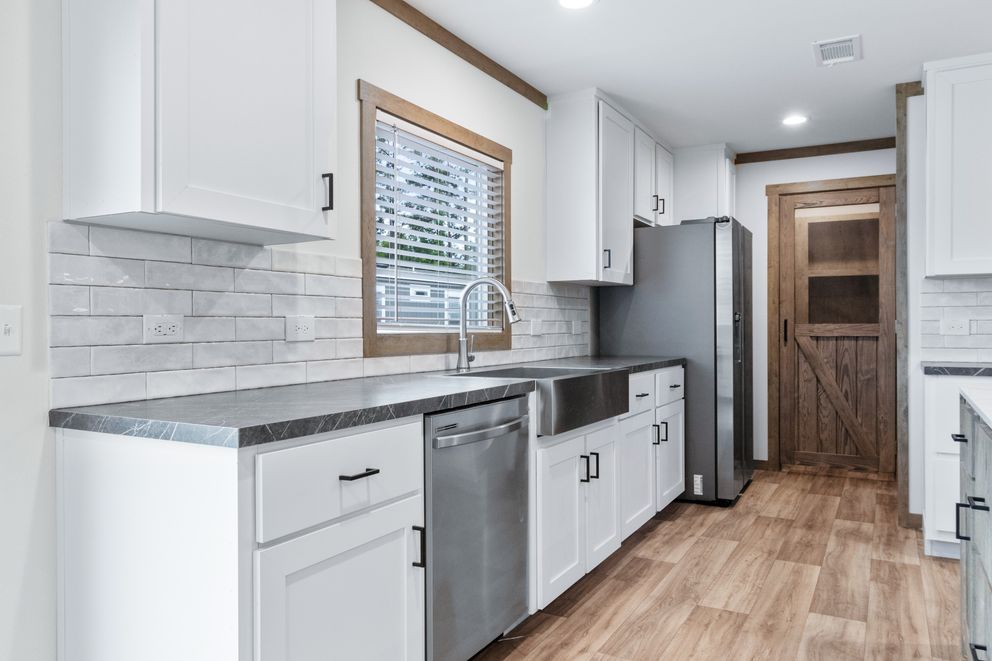 Bright white galley kitchen with stainless steel appliances, gray counters, and wood floors