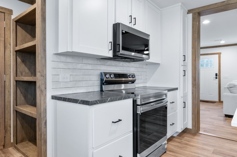 Modern kitchen with white cabinets, stainless steel appliances, and dark countertops opening to a hallway