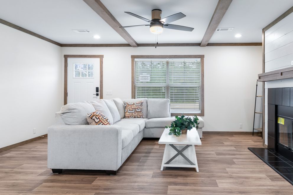 Bright living room with gray sectional, white coffee table, wood floors, ceiling fan, and fireplace.