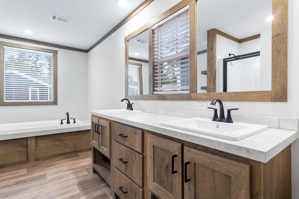Bright bathroom with wood vanity, white countertops, large mirror, and a bathtub by the window.