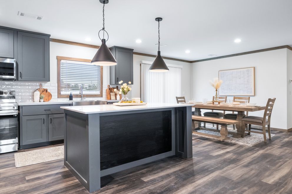 Modern kitchen and dining area with gray cabinets, dark island, pendant lights, and wooden table