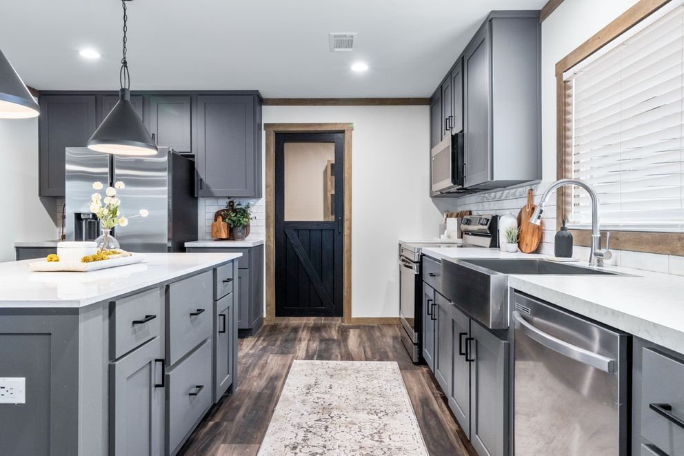 Modern gray kitchen with island, stainless appliances, wood floors, and a window over the sink.