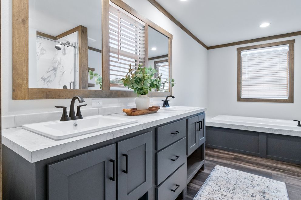 Modern gray bathroom with double vanity, large mirror, and a freestanding bathtub.