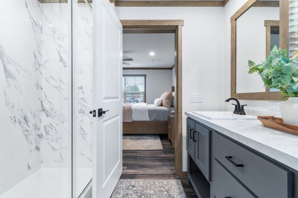 Modern bathroom with marble shower, black vanity, and a doorway to a bedroom beyond