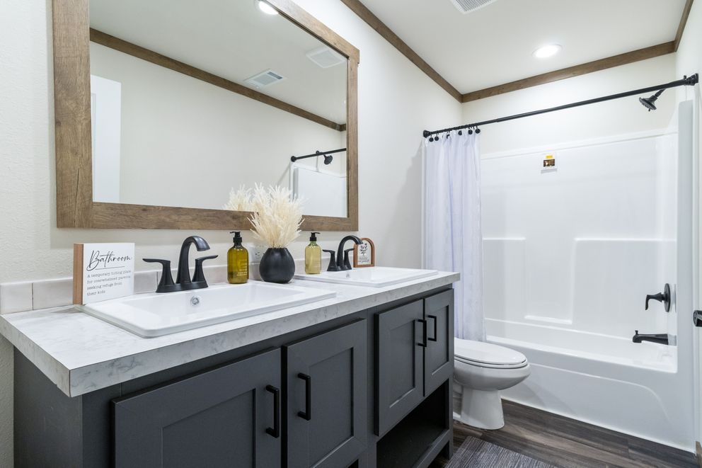 Modern bathroom with dark vanity, large mirror, and white tub-shower combo
