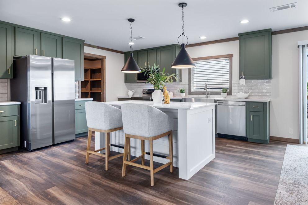 Modern kitchen with green cabinets, stainless steel appliances, white island, and two gray barstools