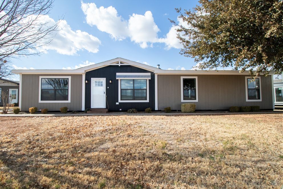 Single-story tan house with white trim, black front door, and a dry front lawn under a blue sky