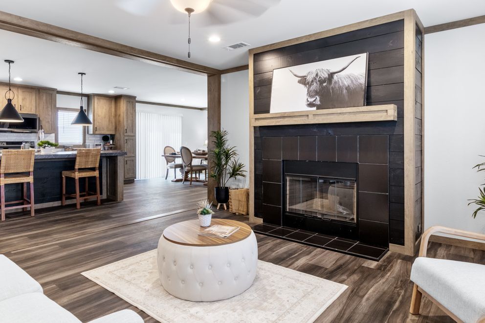 Open-concept living room with fireplace, tufted ottoman, and view into kitchen with island and pendant lights
